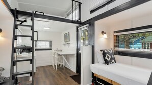 Un apartamento estudio compacto con cama en altillo, kitchenette y una pequeña zona de comedor.