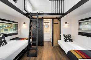Una habitación compacta y moderna con dos camas, una cama estilo litera y un baño pequeño.