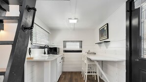 Una cocina compacta con muebles blancos, suelo de madera y una puerta negra.
