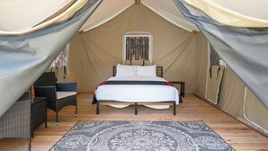 Eine Zelthütte mit einem Bett, zwei Stühlen und einem gemusterten Teppich.