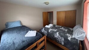 Eine kleine, einfache Unterkunft mit zwei Einzelbetten, einem Holzschrank und einem kleinen Fenster.