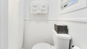 Un bagno con un water bianco, un portascopevoli con due asciugamani, una finestra con persiane e una tenda da doccia.