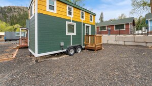 Un piccolo camper a due piani, con esterno verde e giallo, un portico in legno e un rimorchio collegato.