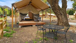 Un espacio al aire libre con toldo, una mesa y sillas, rodeado de árboles y vistas a las montañas.
