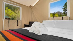 Una cama con toallas blancas enrolladas, una manta a rayas y vistas a árboles y montañas a través de una ventana.