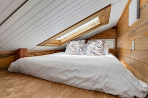 Een slaapkamer met een schuine kap, houten wanden, een bed met gekleurde kussens en een dakraam.
