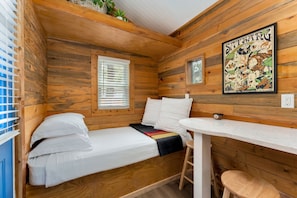 Een kleine hut met een enkel bed, een tafel en een raam.