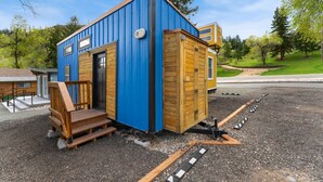 A small, blue and wooden cabin-style building with a wooden staircase and a small porch. - Tiny 2- Sleeping Elephant (Bellvue)