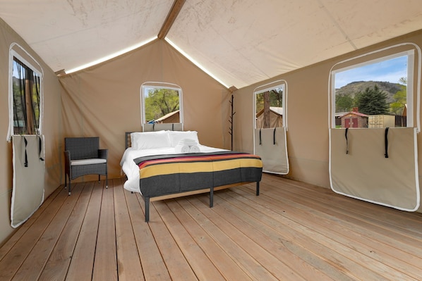 A tented room with a bed, a chair, and two windows.