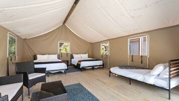 A tented accommodation with two beds, a sofa, and wicker furniture.