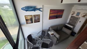 Una habitación con una mesa y sillas de vidrio, un sofá gris, un cuadro de una puesta de sol y una decoración de pez azul en la pared.