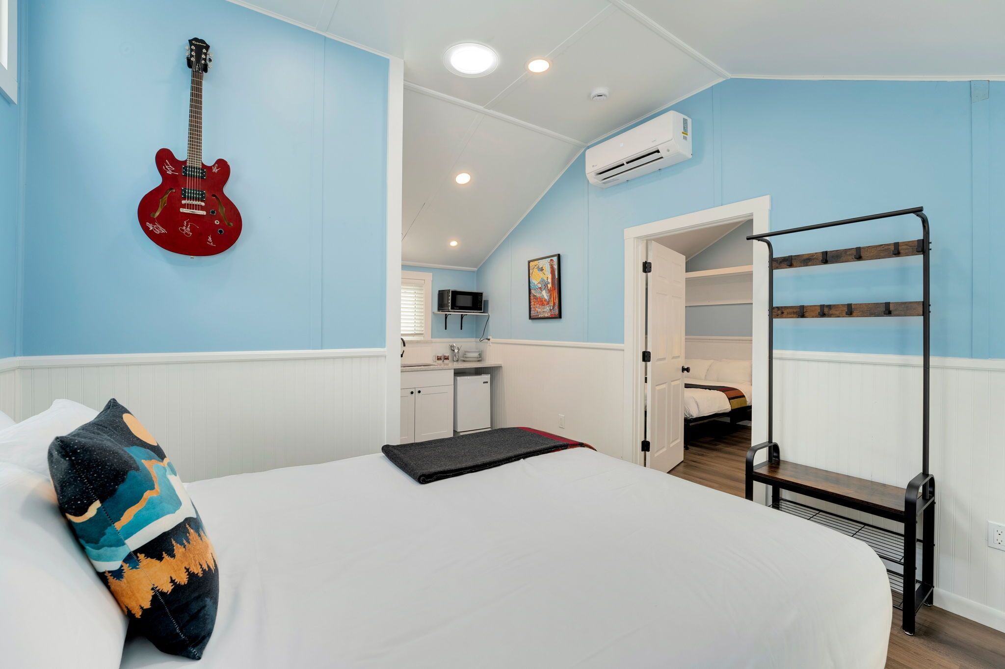 Ein Schlafzimmer mit einem Bett, einer roten Gitarre an der Wand, einem Stockbett und einer Küchenzeile im Hintergrund.