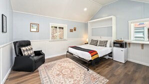 Un dormitorio con cama, una silla, una mesita y un microondas.