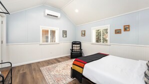 Un dormitorio con una cama, una silla, un ventanal y un equipo de aire acondicionado.