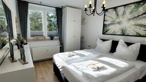 Quarto com duas camas, janela com cortinas, radiador, candelabro e um quadro na parede.