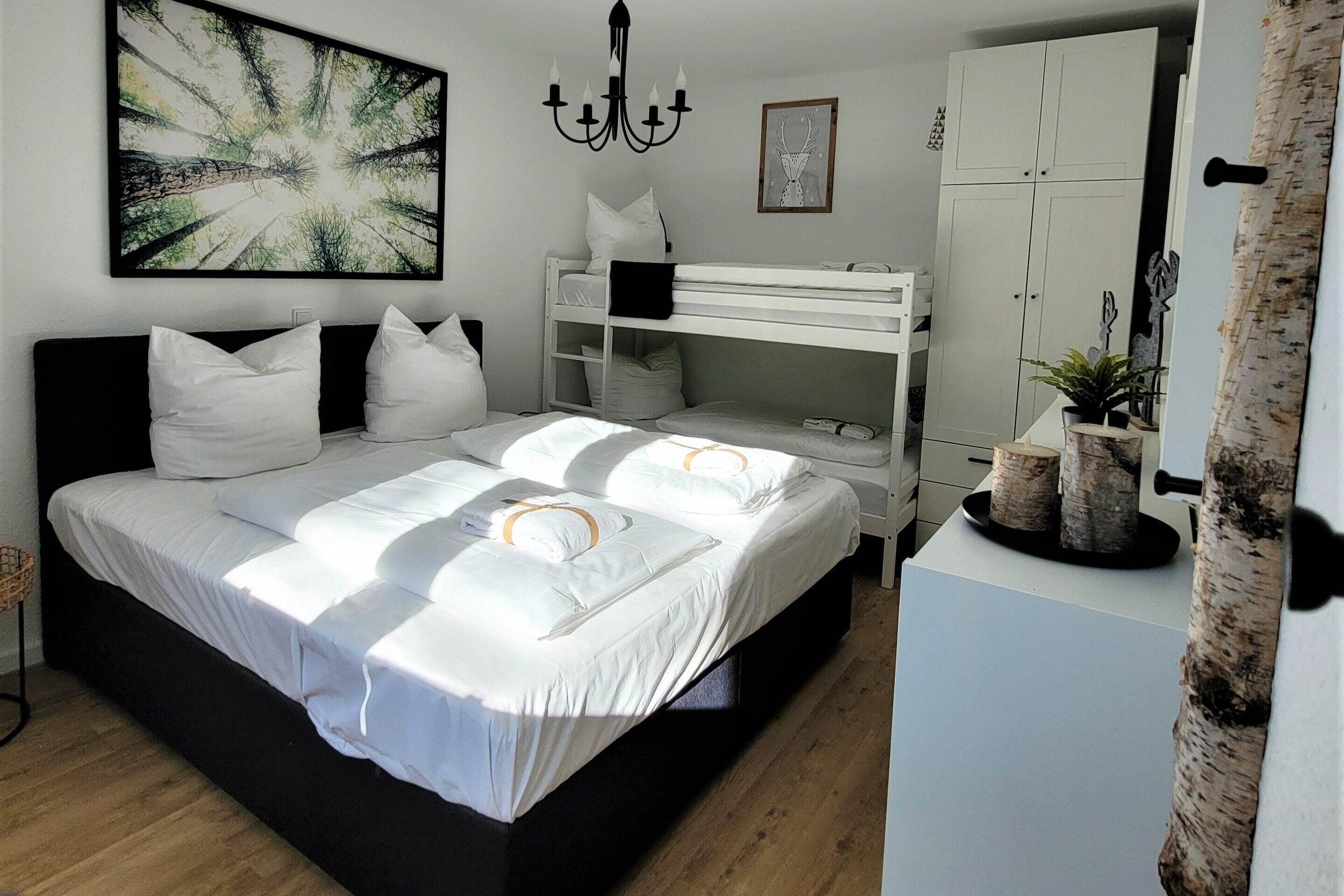 A bedroom with a large bed, a bunk bed, a chandelier, a wardrobe, and a painting on the wall.
