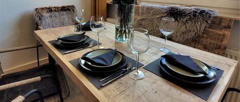 A dining table set with plates, cutlery, and wine glasses, flanked by chairs with fur throw pillows.