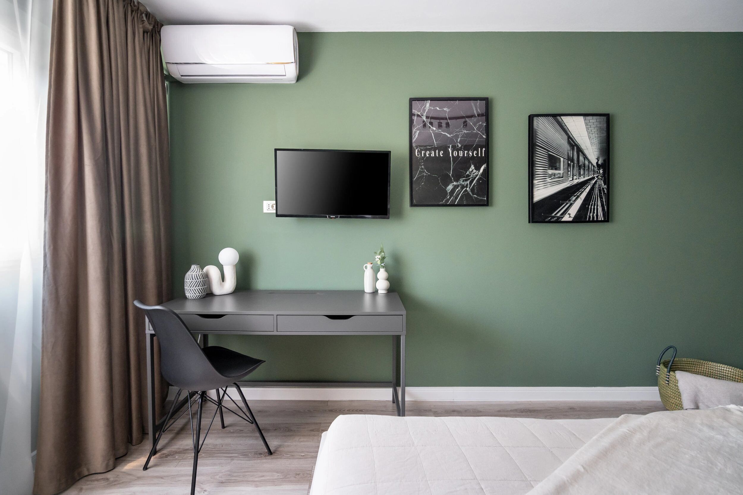A modern hotel room with a green wall, a flat-screen TV, a desk with a chair, and two framed pictures.