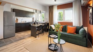 A modern kitchen with dark cabinets, a built-in oven, and a dining area with a table and chairs. There is a green sofa with orange cushions and a small side table with a vase and magazine. - Artful & Light-Filled 2BR on Calea Victoriei - Prime Central Spot (Bucharest)