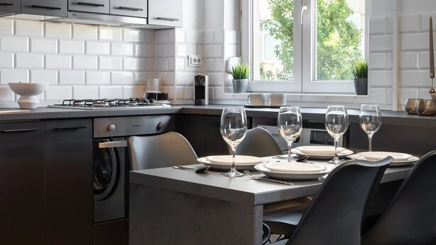 A modern kitchen with dark cabinets, a central island with seating, and a window providing natural light. - Artful & Light-Filled 2BR on Calea Victoriei - Prime Central Spot (Bucharest)