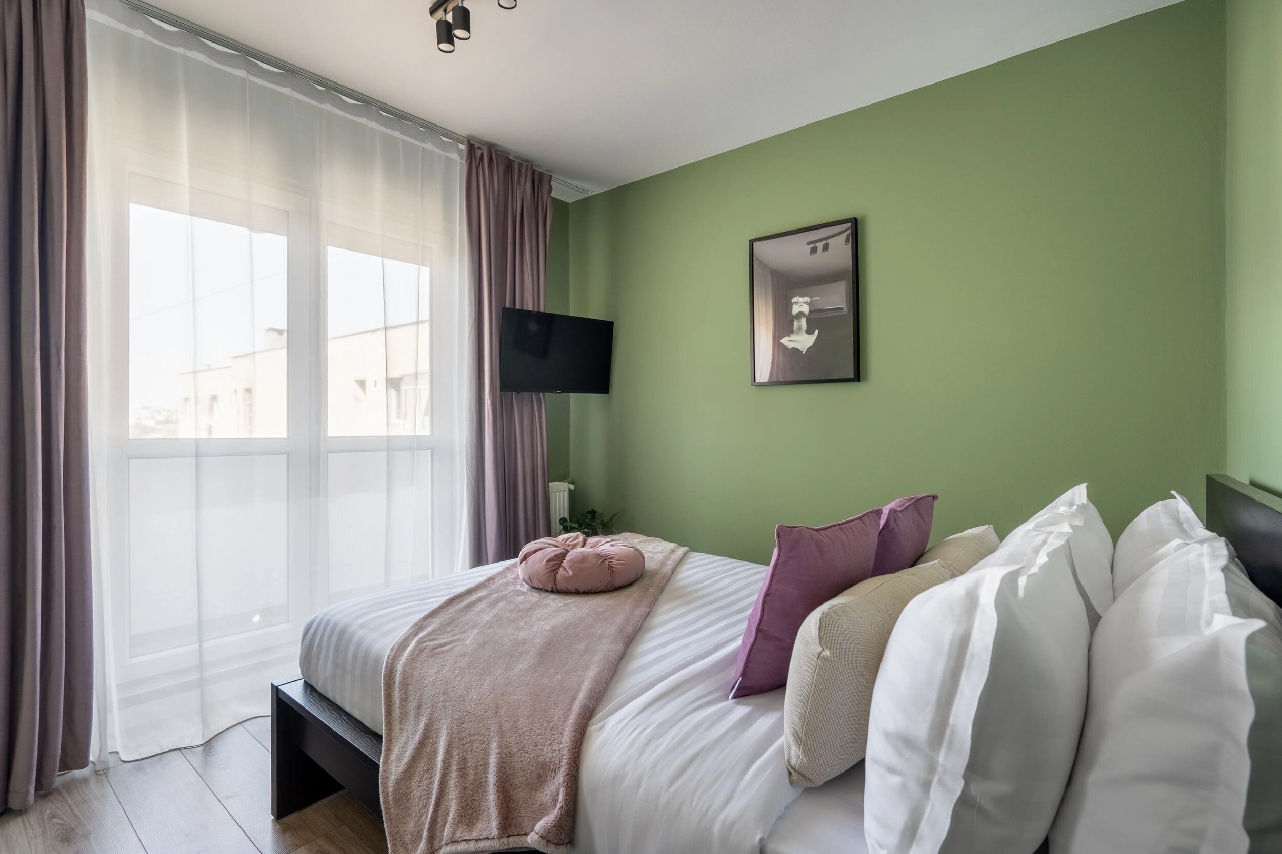 A bedroom with a bed, a TV, and a window with curtains.