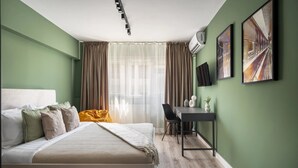 A bedroom with a bed, a desk, and a chair. There is a window with curtains, a wall-mounted air conditioner, and two framed pictures. - Artful & Light-Filled 2BR on Calea Victoriei - Prime Central Spot (Bucharest)