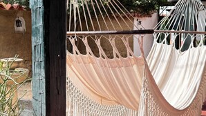 A hammock hanging between two wooden posts, with a rustic wall and potted plants in the background.