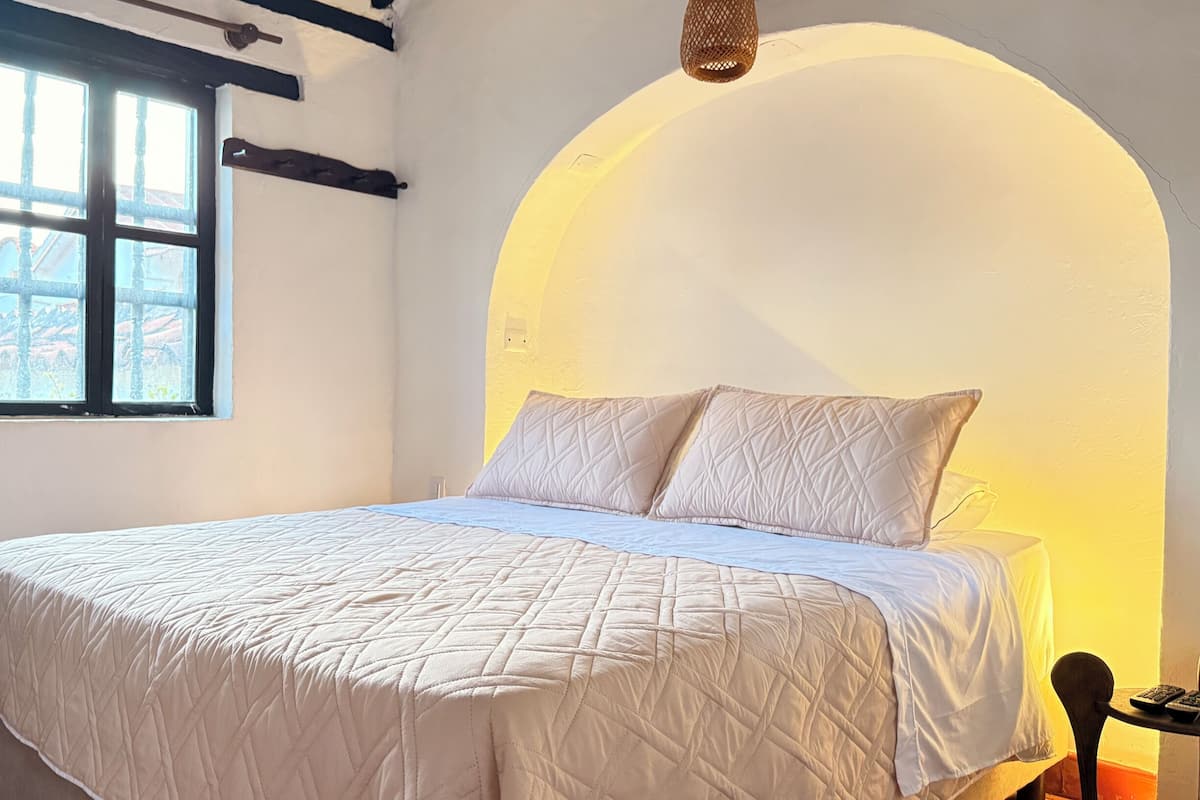 A bed with a quilted white duvet, a window with curtains, and a wall with a circular arch.