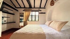 A bedroom with a bed, a window with curtains, a mirror, and wooden beams on the ceiling.