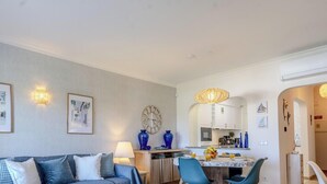 Un salon moderne avec un canapé, une table à manger et des chaises. On y trouve également un coin cuisine avec des placards et une horloge au mur.