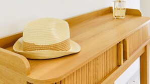 A wooden console table with a woven hat and a bottle of perfume.