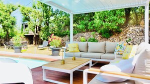 A covered outdoor seating area with a pool, a stone wall, and lush greenery.