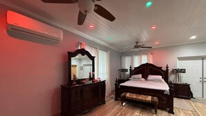 A bedroom with a wooden floor, a large bed with a headboard, a dresser, a ceiling fan, and an air conditioning unit. - Luxurious and Charming 3-bedroom house with WiFi, AC in delightful George Town (George Town)