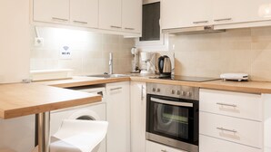 Une cuisine moderne avec des meubles blancs, un four en acier inoxydable, une machine à café et un lave-linge.