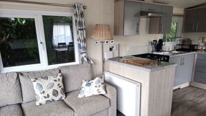 Un espacio habitable compacto con sofá, una pequeña zona de cocina y una ventana con cortinas.