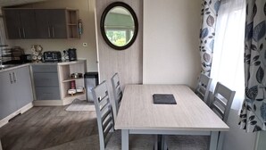 Cocina compacta con gabinetes grises, un lavamanos pequeño y una cafetera. Hay una mesa de comedor con cuatro sillas y un espejo encima.