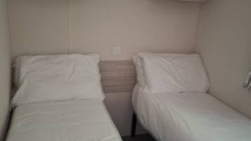 A small, single-room accommodation with two beds, a wooden wardrobe, and a single light switch on the wall.