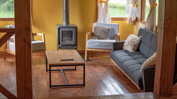 Ein gemütliches Zimmer mit Holzboden, einer Couch mit Kissen, einem kleinen Tisch und einem Kaminofen.