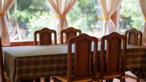 Ein Essbereich mit Holztischen und -stühlen, drapiert mit weißen Vorhängen, die mit gelben Bändern gebunden sind.