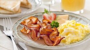 Un plato de desayuno con tocino, huevos revueltos, fresas y un vaso de jugo de naranja.