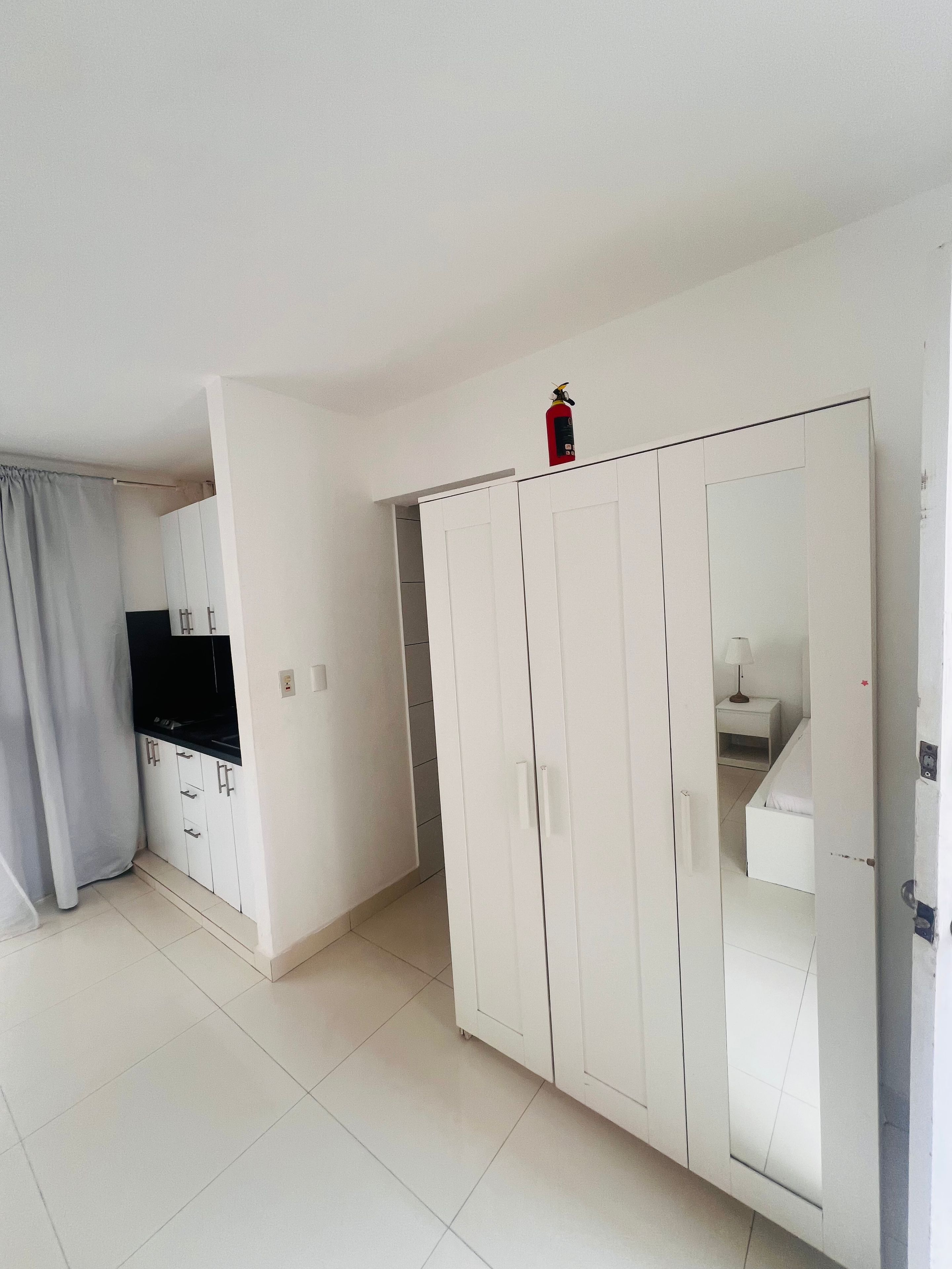 Una habitación con armario, cama, mesita de noche y ventana con cortina.