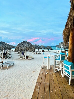 A beachside area with thatched umbrellas, lounge chairs, and a wooden deck. - Paradise Beach Suites Sol Caribe (Punta Cana)