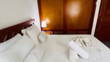 Une chambre d’hôtel avec un grand lit, une tête de lit en bois, une table de chevet avec une lampe et une armoire.