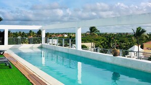 A rectangular swimming pool with a wooden deck and a grassy area on one side. - Ducassi Rooftop Pool Beach Suites (Punta Cana)