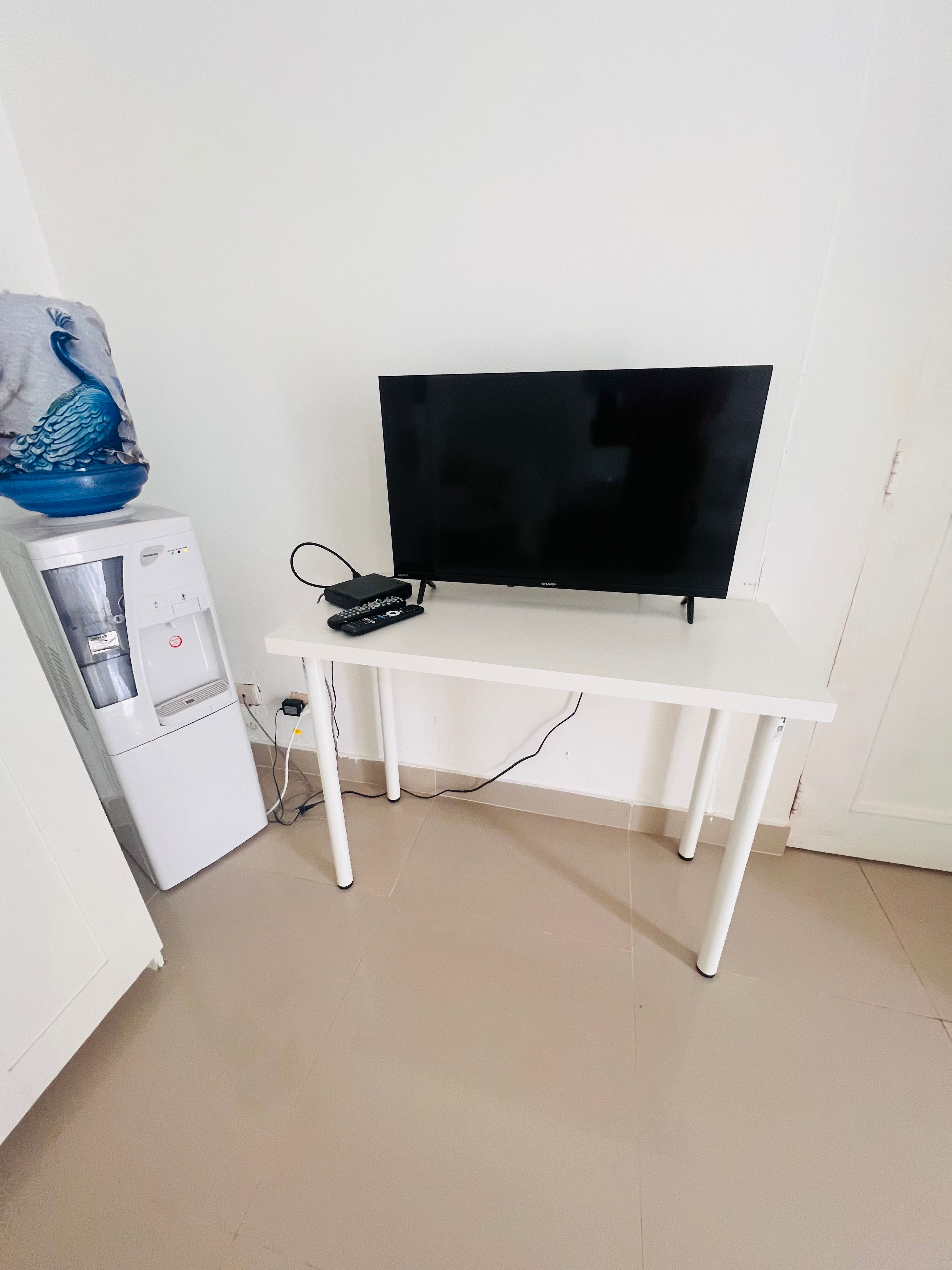 A white desk with a flat-screen TV, a water dispenser, and a remote control on the floor.