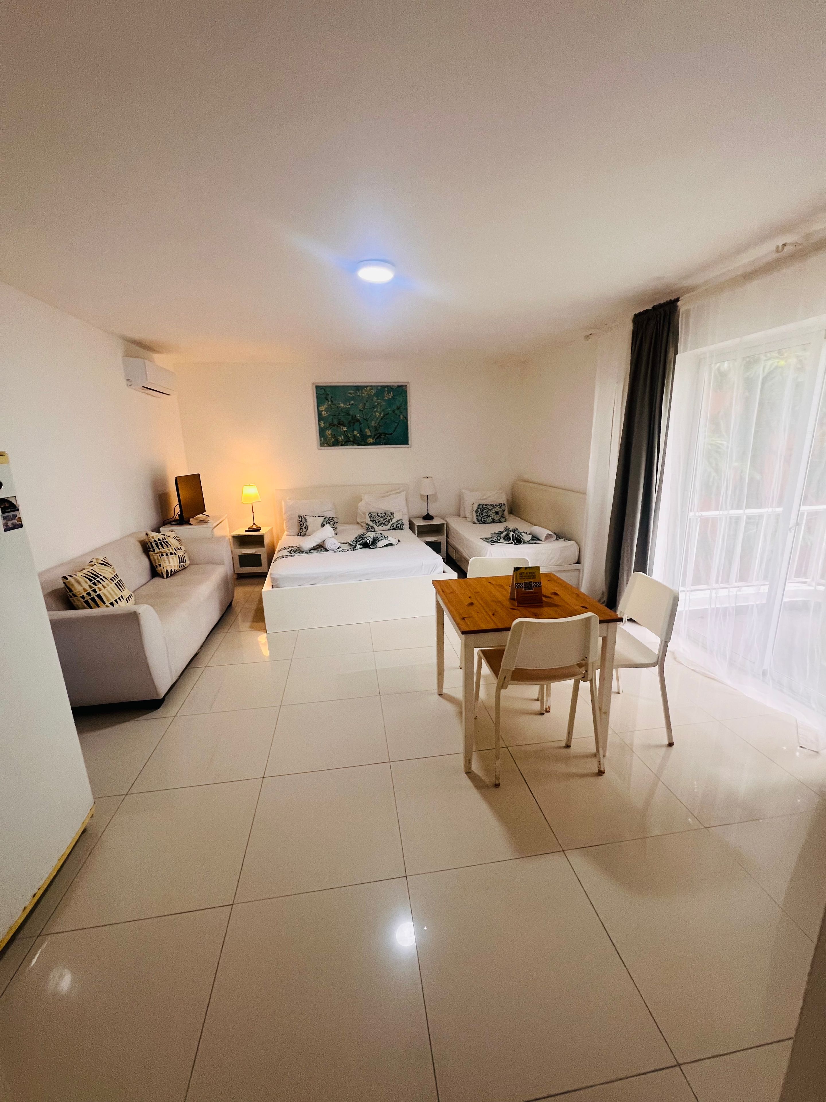 Une chambre d’hôtel avec un lit, un canapé, une table et des chaises. Il y a une fenêtre avec des rideaux.