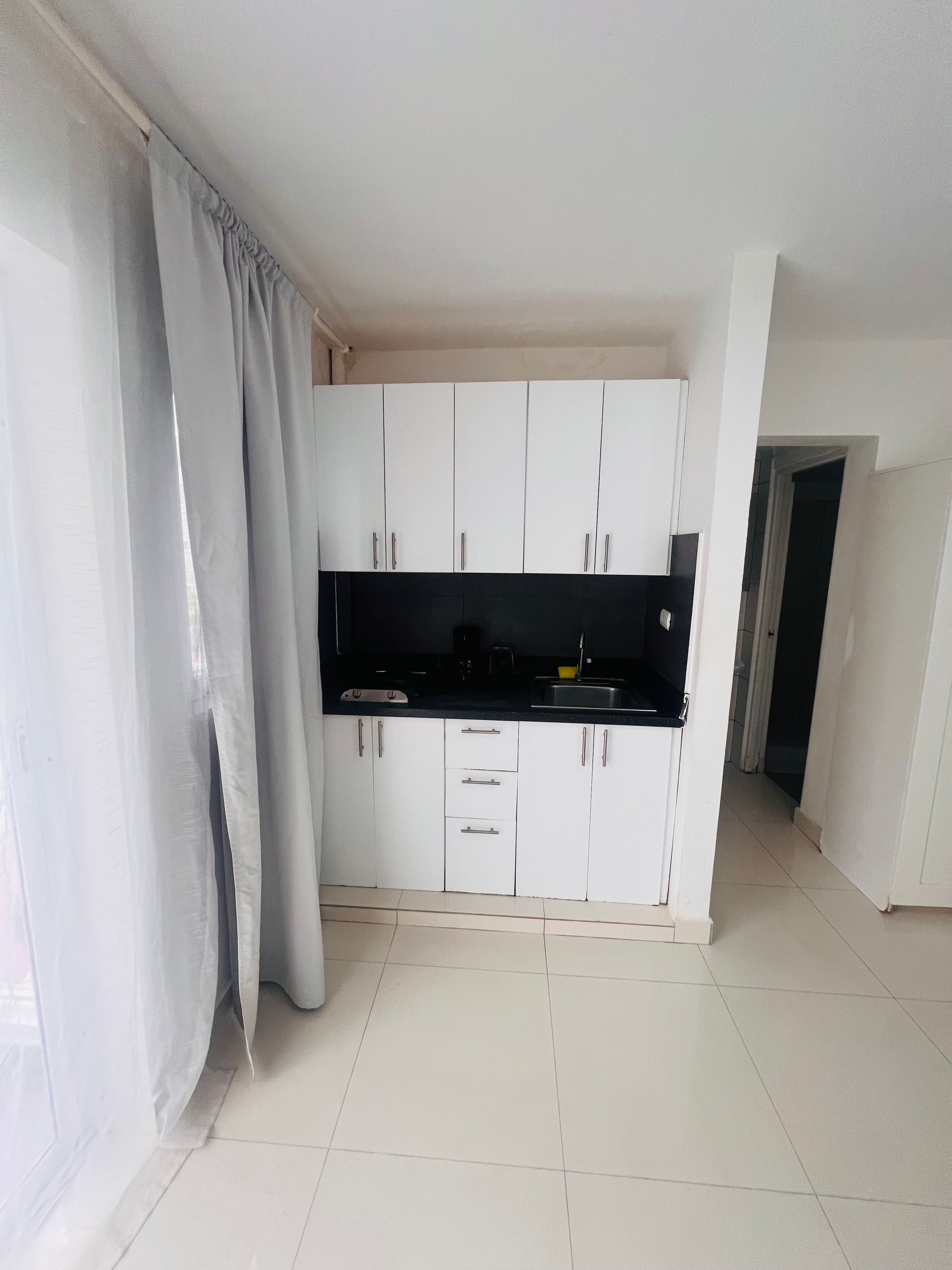Cozinha com armários brancos, bancada preta e piso ladrilhado.