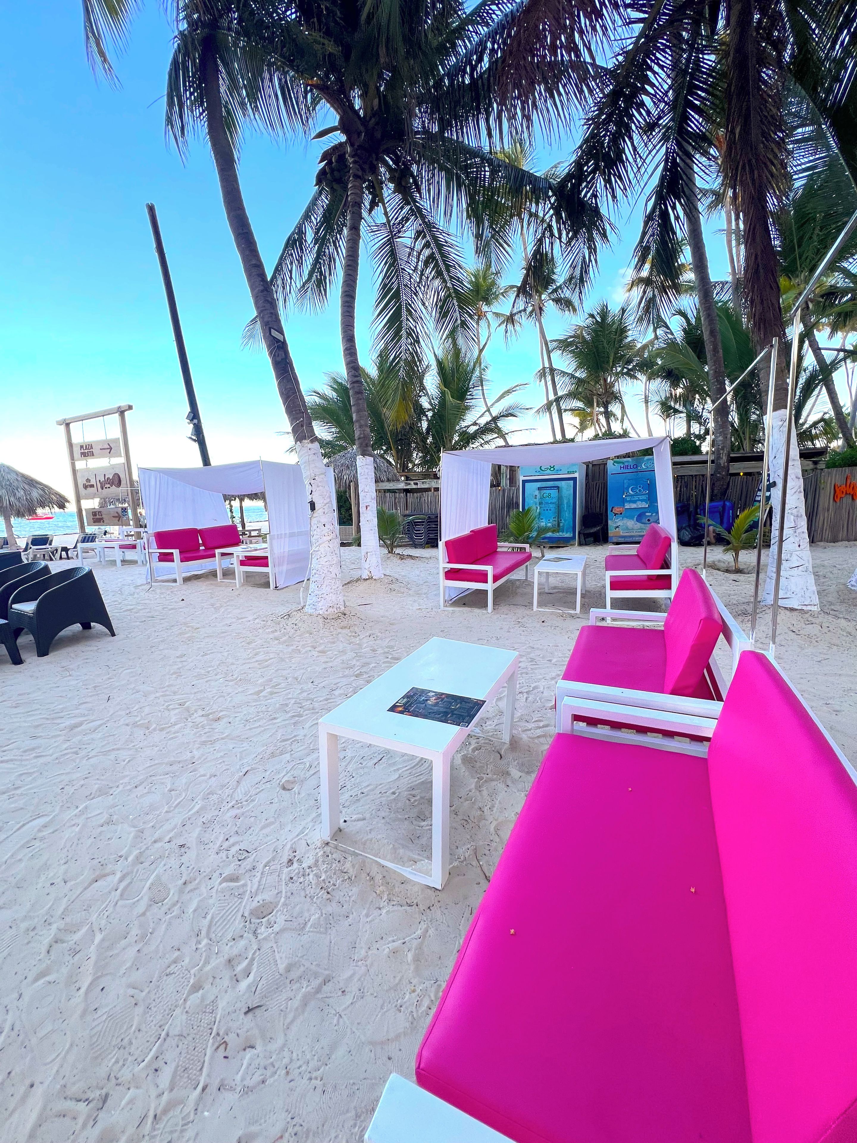 A beachside lounge area with white and pink seating, a small table, and a tent structure.