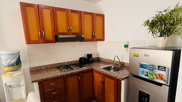 Cocina compacta con armarios de madera, un refrigerador de acero inoxidable y una encimera con lavamanos.