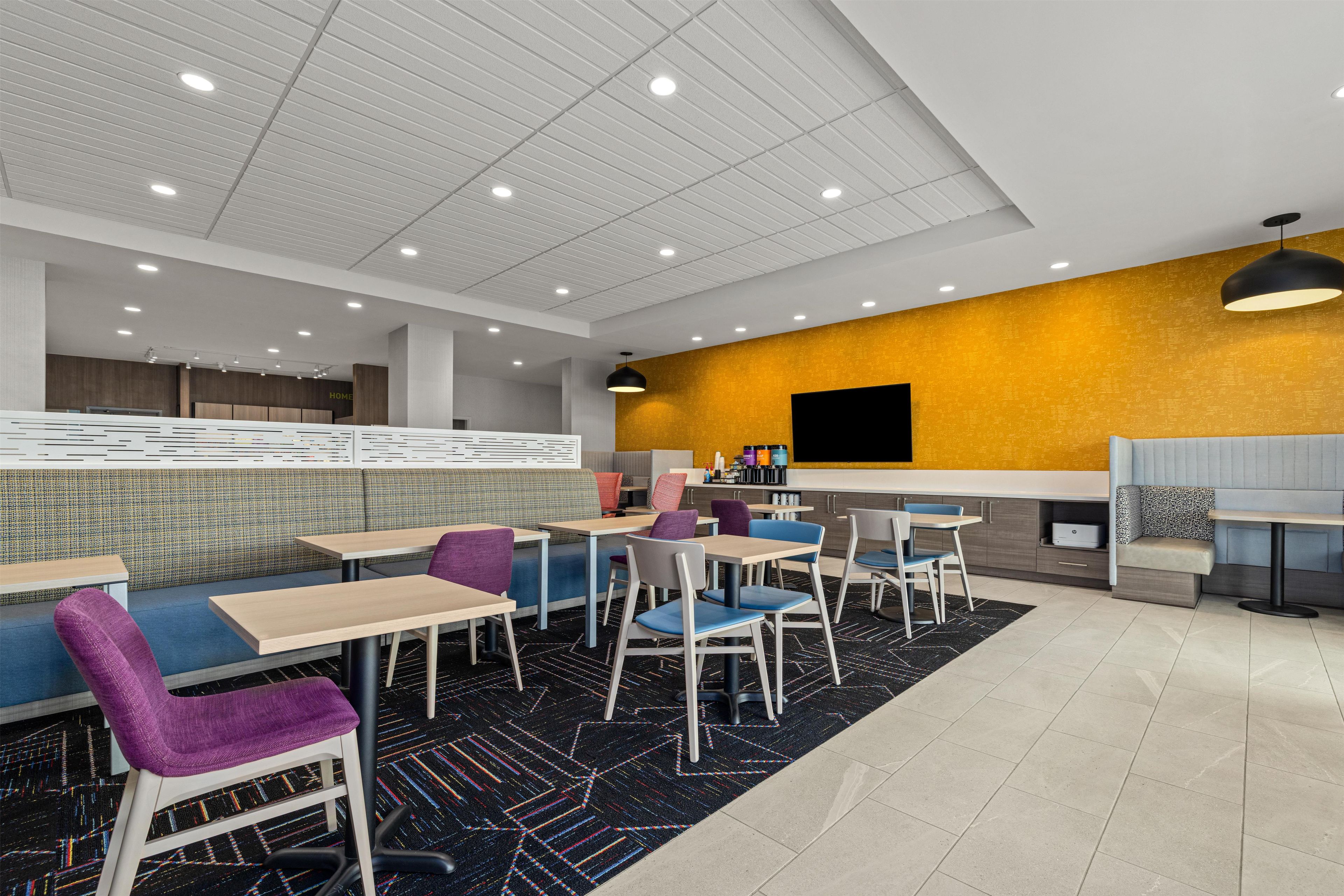 A modern restaurant with booths and tables, a yellow accent wall, and a black ceiling.